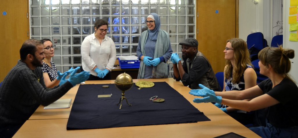 Group of volunteers sitting and standing around a table looking at brass astronomical instruments. 